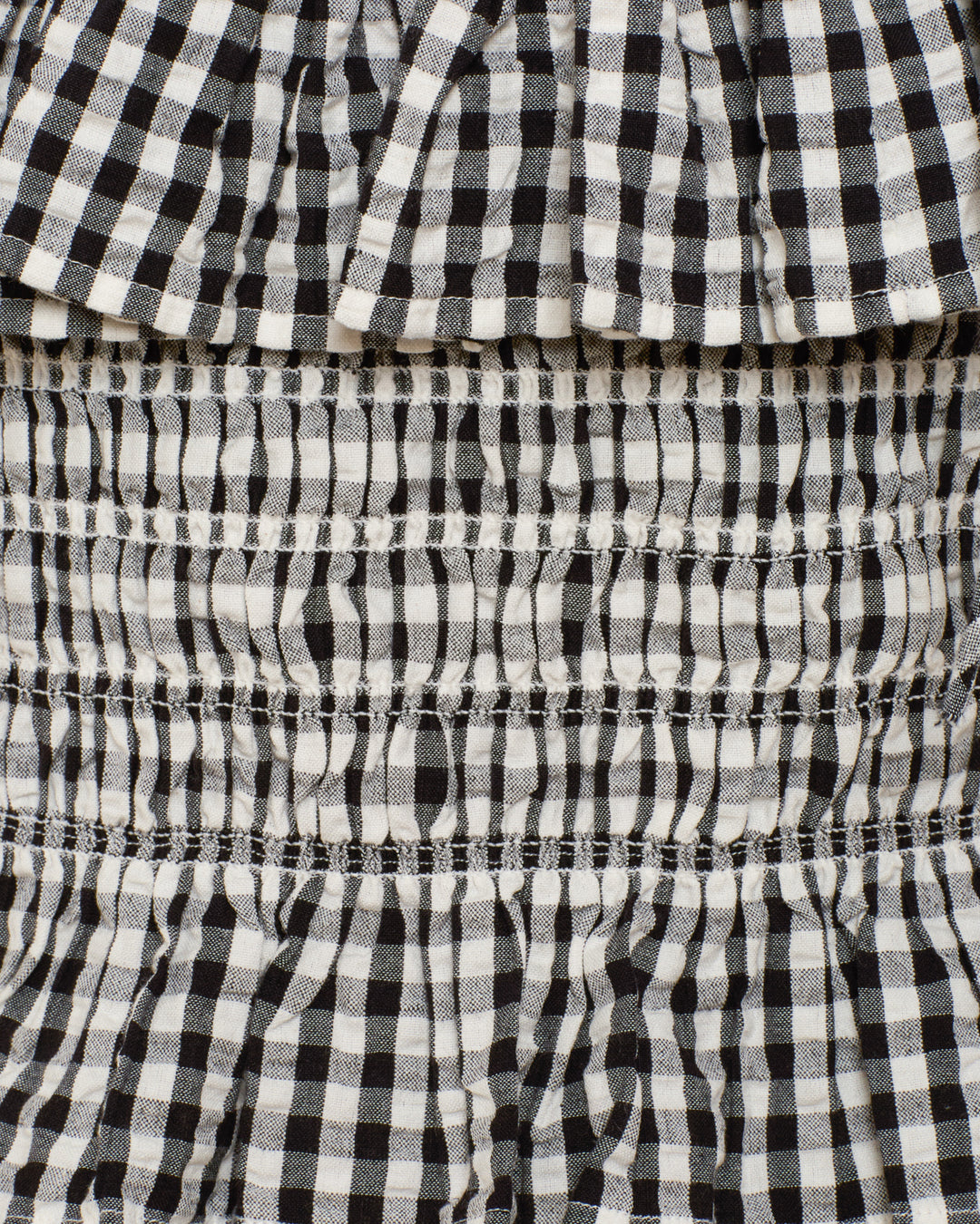 Close-up of the Clara Sideshow Check Top, showcasing black and white gingham fabric with gathered, ruched, and ruffled details and a peplum hem.