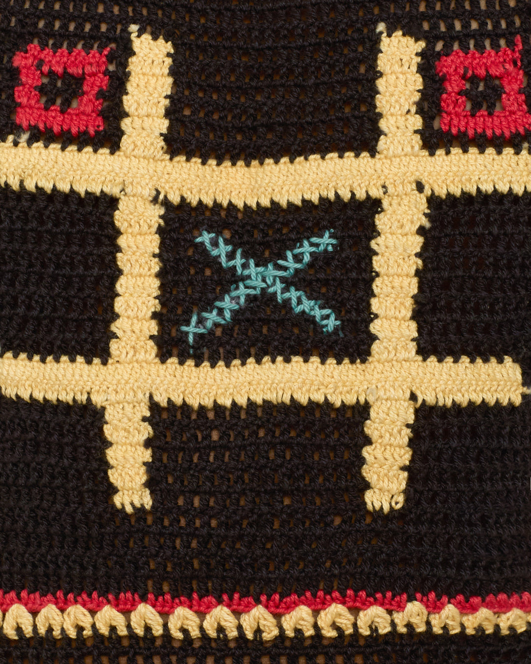 Close-up of the Elide Tic Tac Toe Top, an artisan-made crocheted board featuring a yellow grid, red circles, and a blue "X" in the center on a black background.