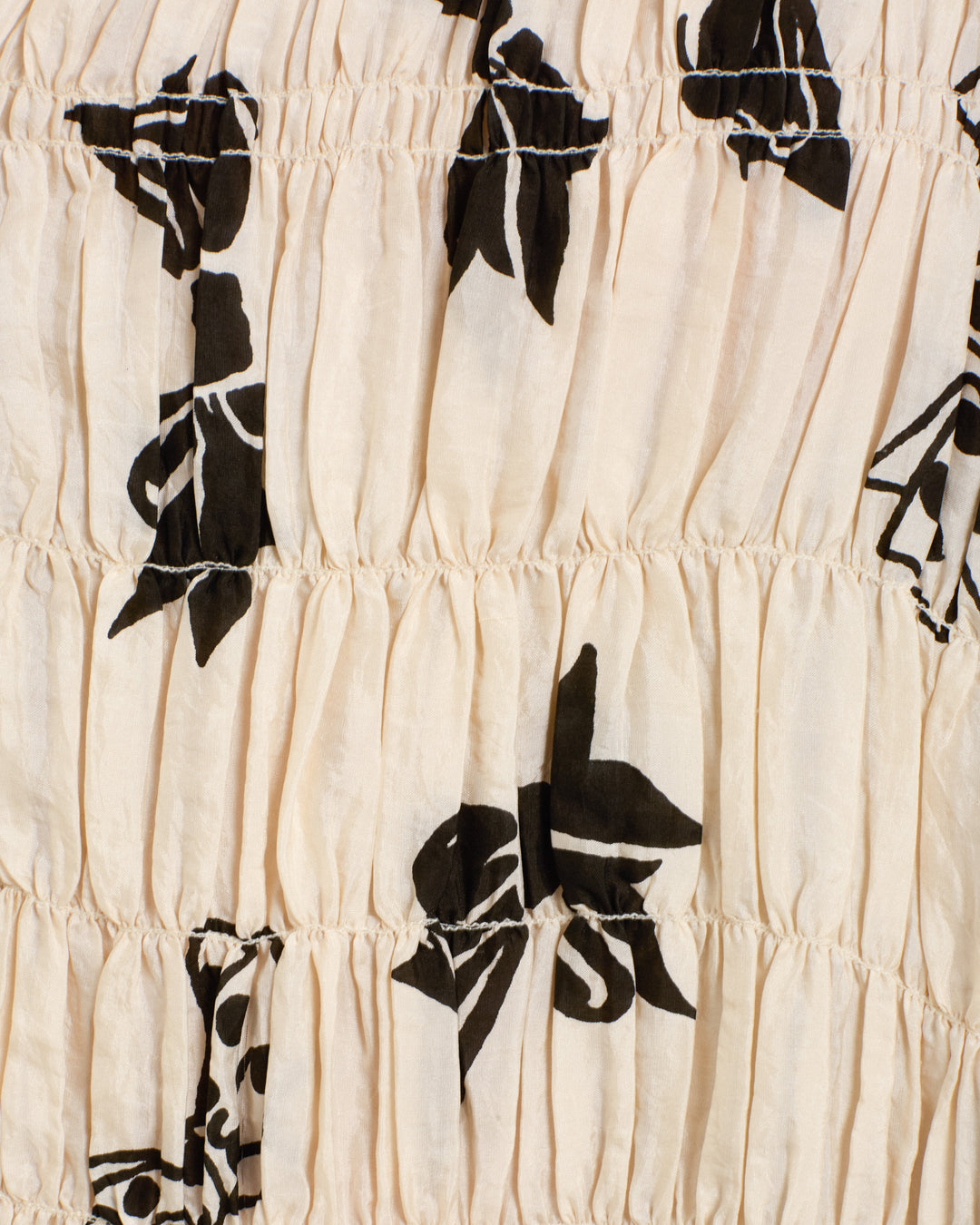 Close-up of the Ellina Black Tie Silk Dress, featuring light beige silk fabric with black abstract floral or leaf prints in a repeating block-printed pattern and elegant gathered detailing.