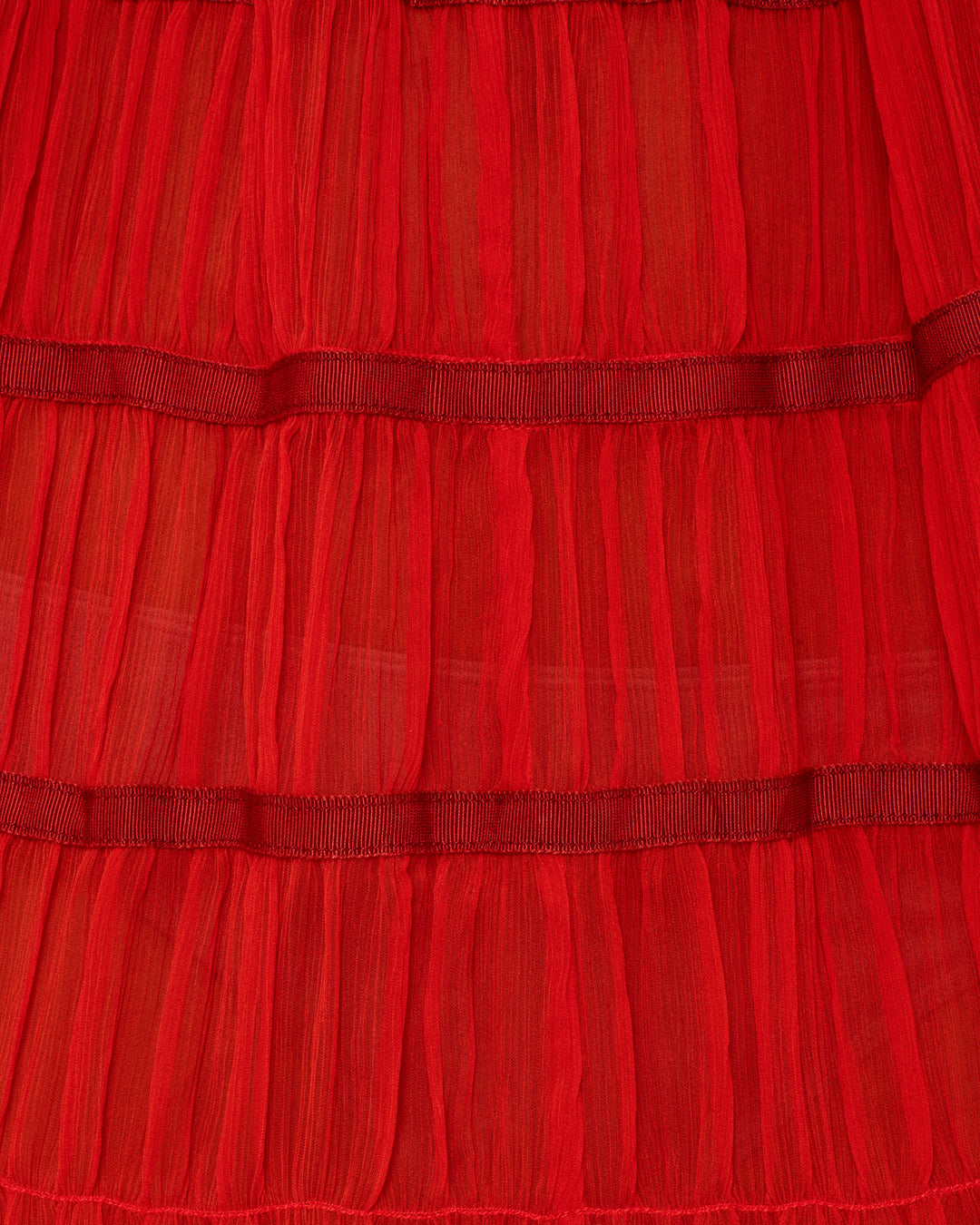 Close-up of the Emrys Ibis Chiffon Dress, showcasing layered red chiffon with horizontal pleats, textured stitching, and subtle ruched tiers.