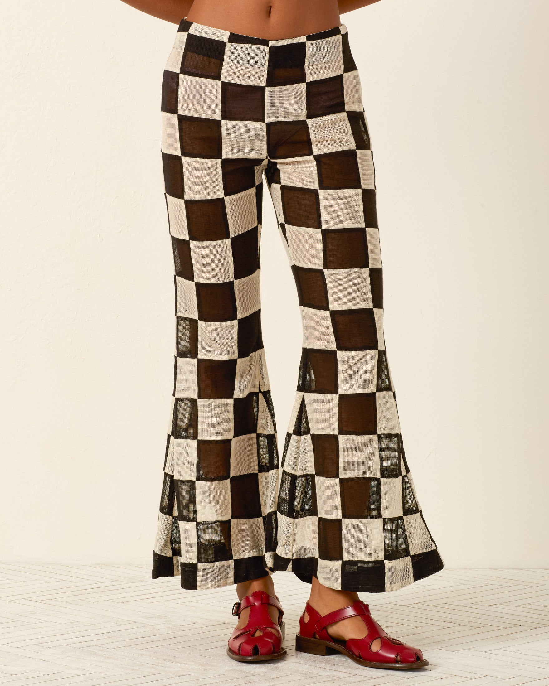Person wearing the Farah Harlequin Pant with a black and white checkered bell-bottom flare design and red sandals, standing on a light patterned floor against a plain background.