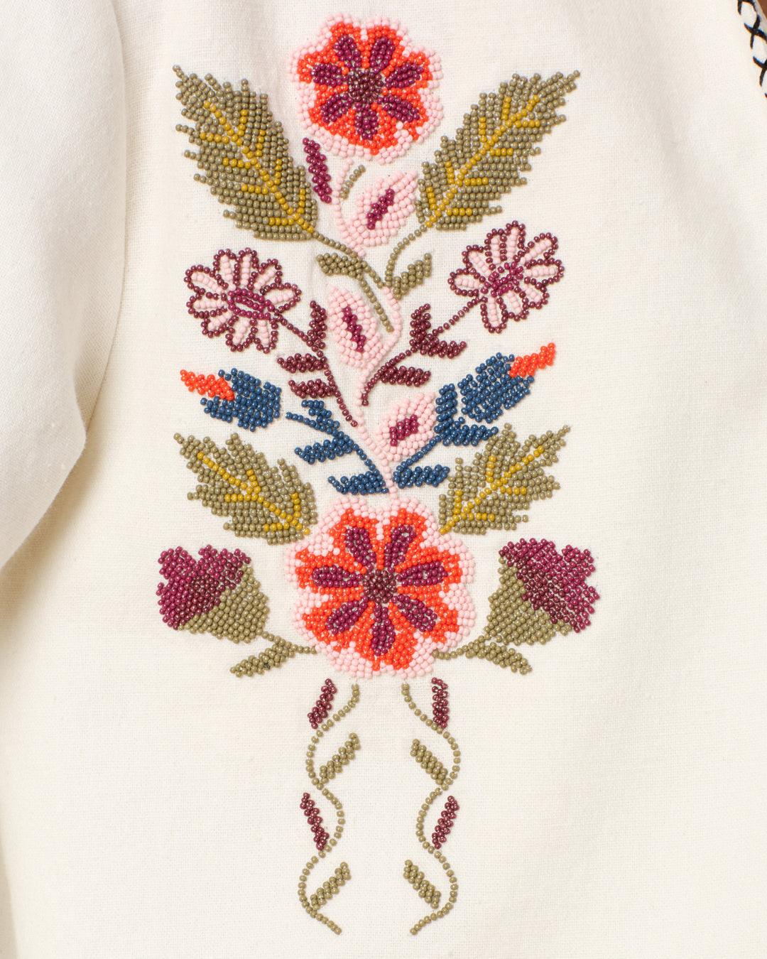 Close-up of the Francis Heirloom Flora Jacket's white textured cotton fabric, featuring vibrant red, pink, green, and blue floral and leaf embroidery.
