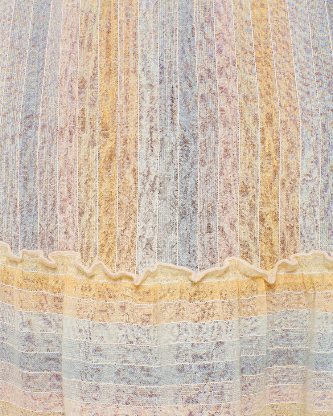 Close-up of the Ida Sunwash Stripe Dress, a lightweight cotton dress with vertical pastel stripes in blue, pink, yellow, and cream, featuring a ruffled seam near the bottom.