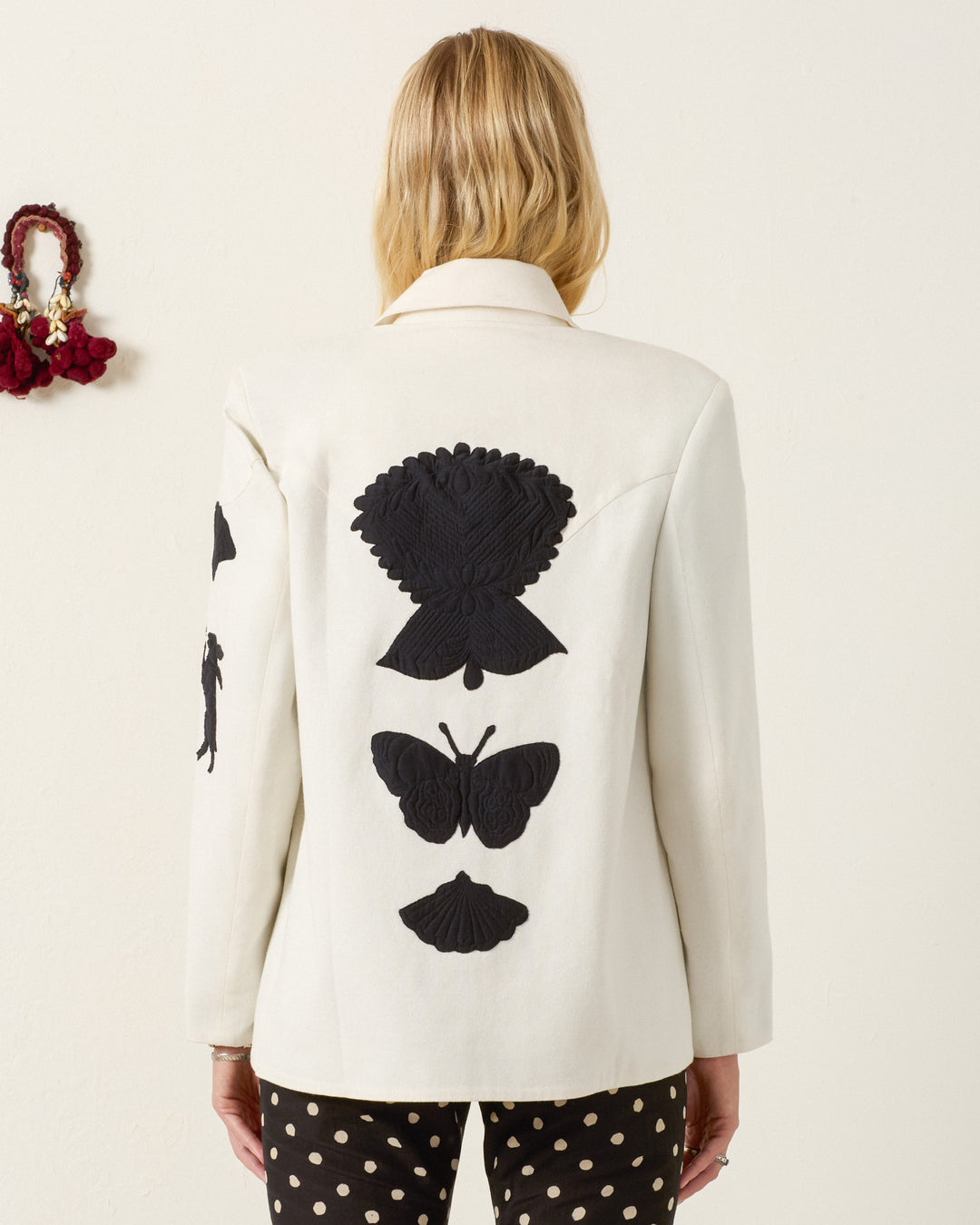 A person wearing the Jude Pearl Reverie Jacket, featuring textured cotton and black butterfly appliqués on the back, paired with black polka dot pants, facing away from the camera.