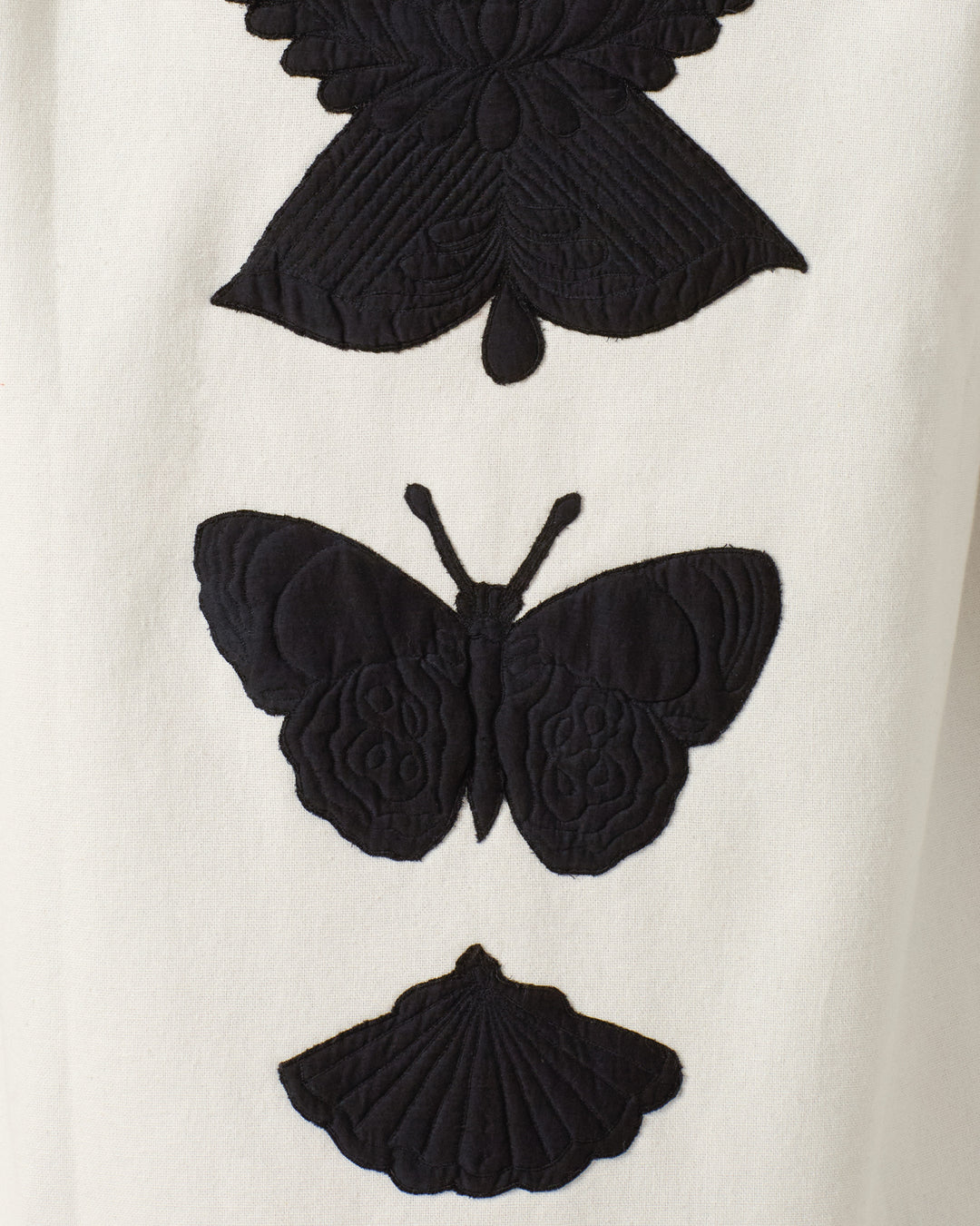 Three black embroidered insects, resembling moths or butterflies, are arranged vertically on a white appliqué, adding striking detail to the textured cotton Jude Pearl Reverie Jacket.