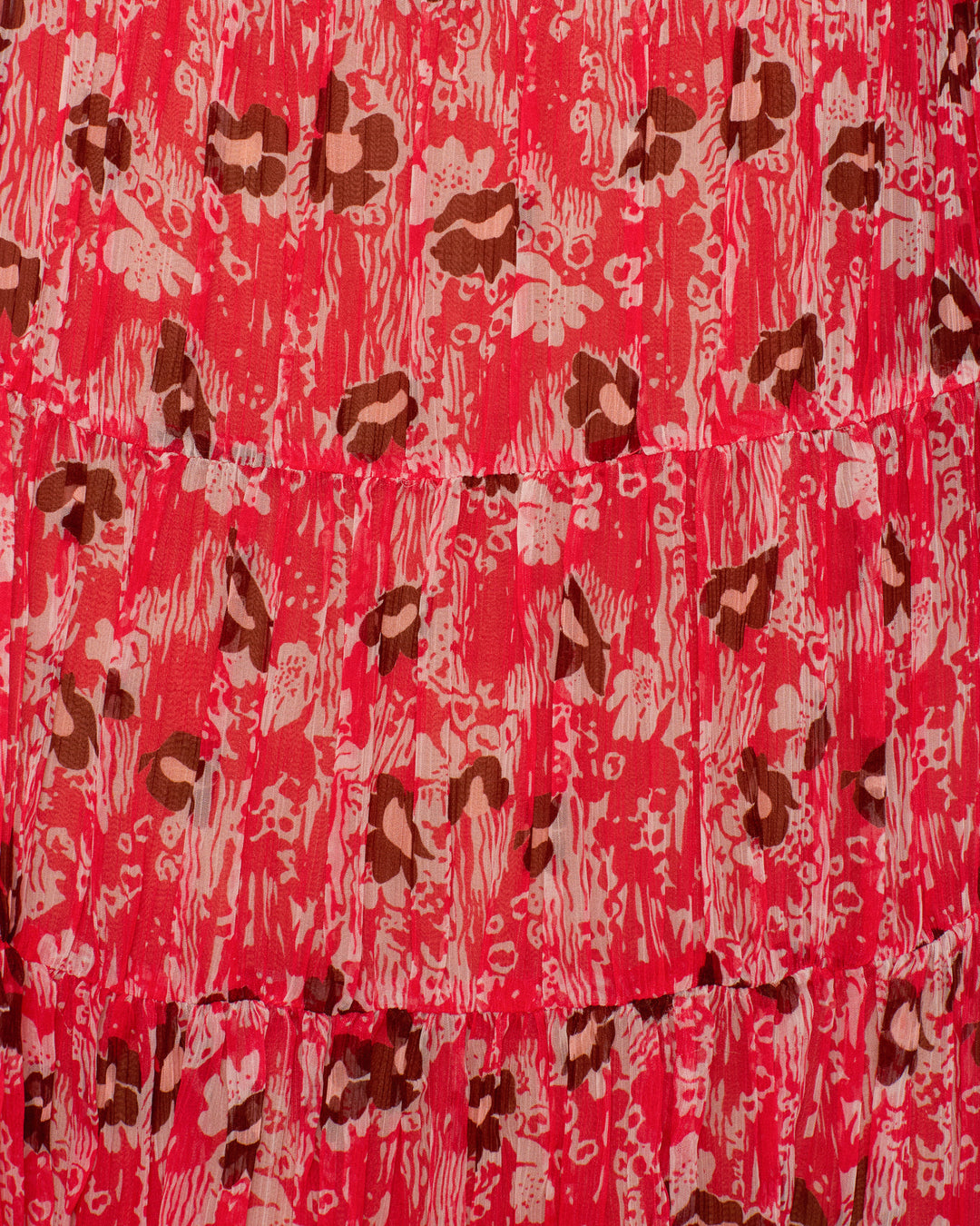 Close-up of the Jule Rougewood Dress crafted from cupro-chiffon, showcasing a red and pink backdrop with irregular brown and light pink animal prints and visible horizontal stitching.