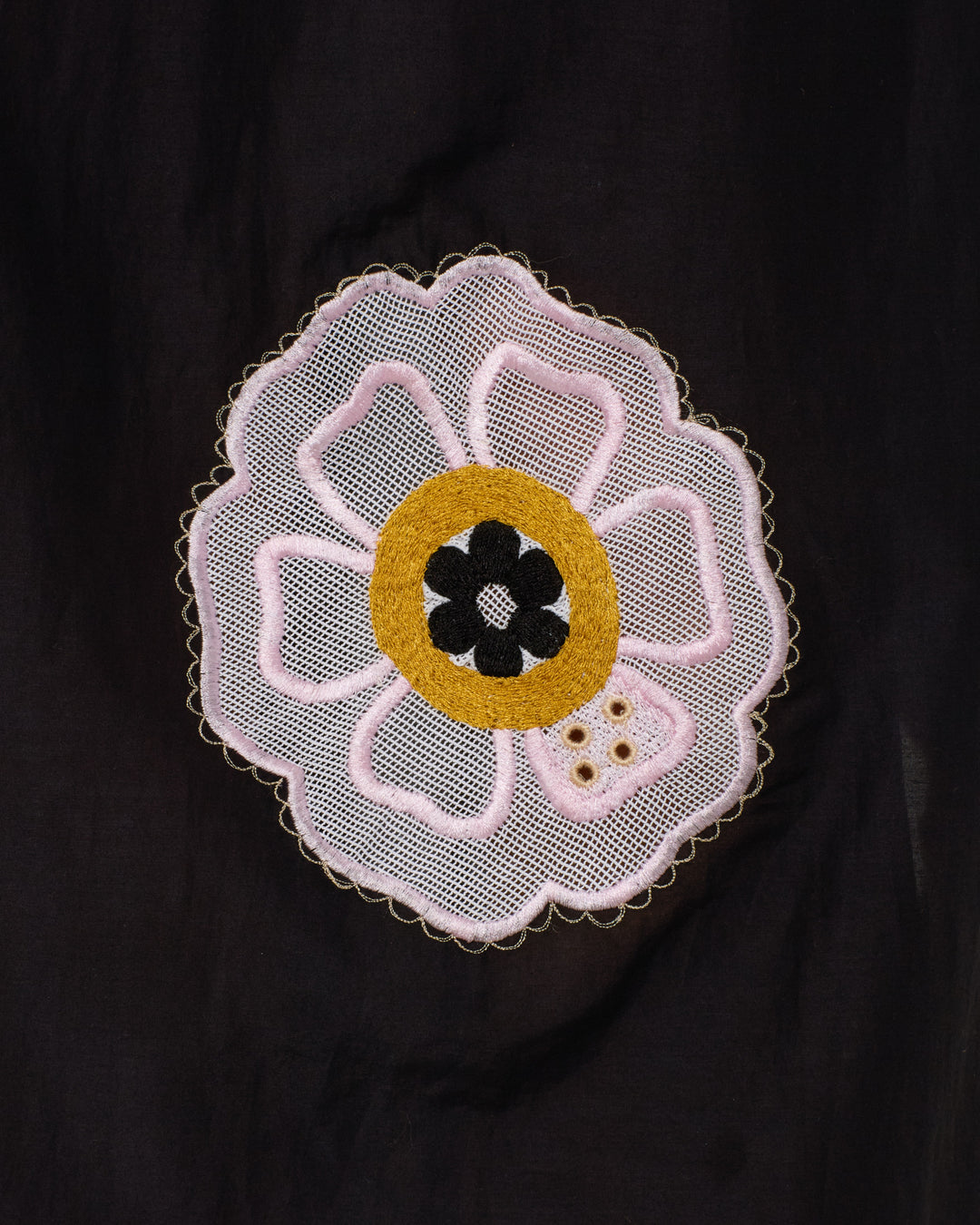 The Lilia Pressed Daisy Dress features a decorative embroidered patch with a floral design in white, yellow, and black on a black background—perfect for adding charm to this empire-waist cotton-silk blend dress.