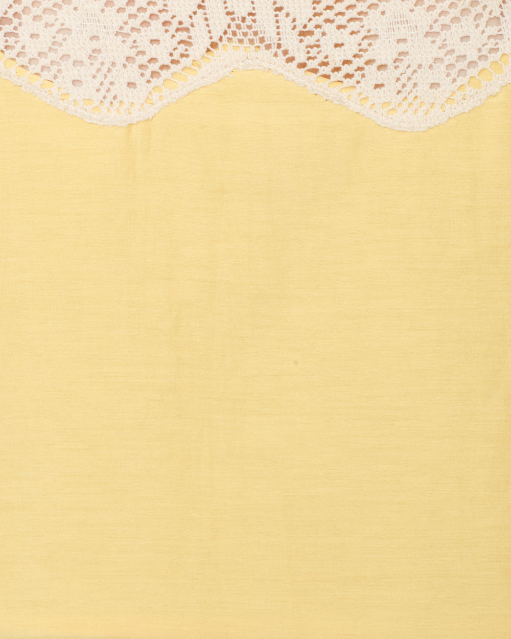 White lace fabric with a scalloped edge drapes over a plain, light yellow background, evoking the refined charm of the Mia Maize Prima Lace Top—its delicate cotton-silk blend and lace-trimmed detailing perfect for an elegant sleeveless look.