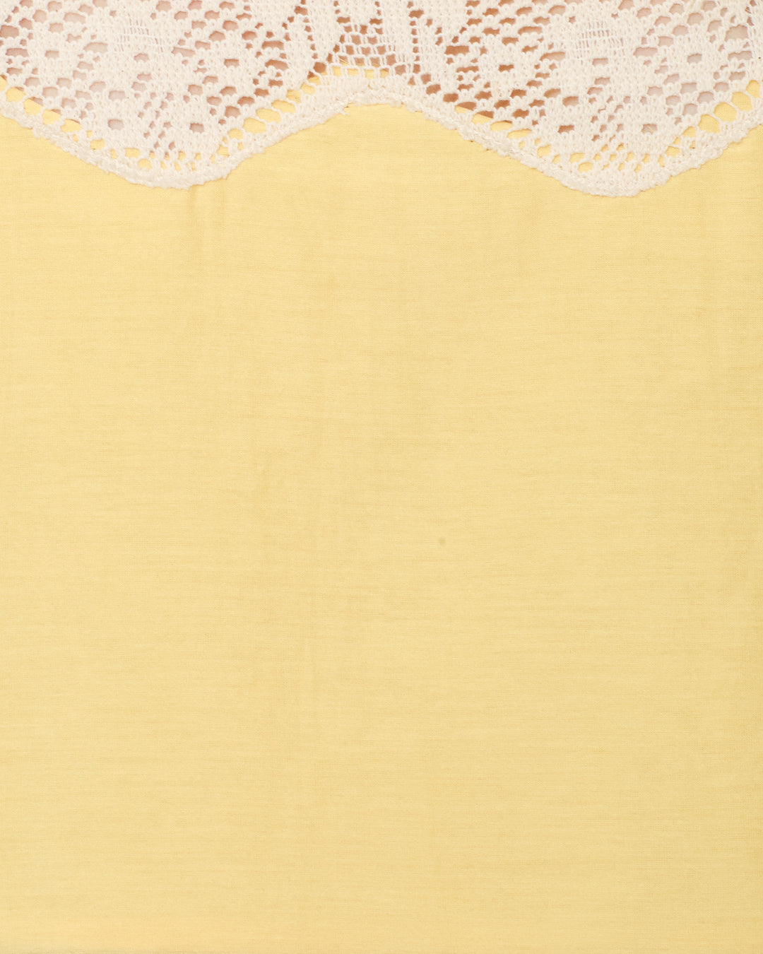 White lace fabric with a scalloped edge drapes over a plain, light yellow background, evoking the refined charm of the Mia Maize Prima Lace Top—its delicate cotton-silk blend and lace-trimmed detailing perfect for an elegant sleeveless look.