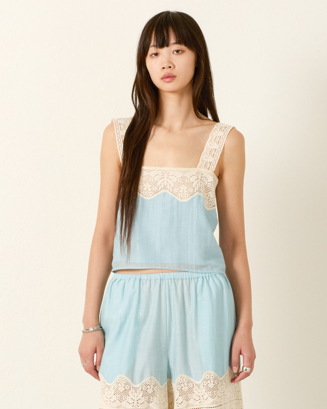 A woman with long straight hair wears the Mia Sky Prima Lace Top and matching shorts with cream lace trim, creating a fresh summer look against a plain light background.