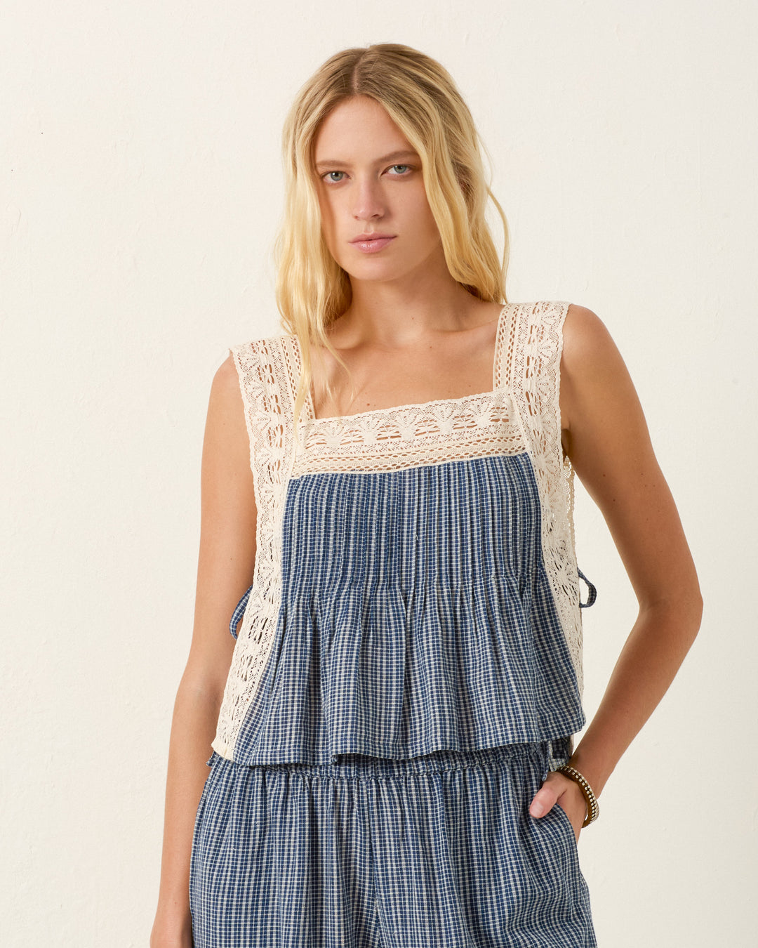 Woman wearing the Mimi Prima Micro Plaid Top in blue Khadi cotton with delicate lace trim, standing against a plain off-white background.