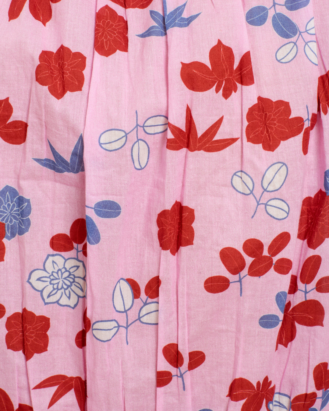 The Nova Tutu Bloom Shirt features pink fabric with red and blue floral patterns, vertical pleats, and airy cotton voile—perfect for a breezy blouse look.