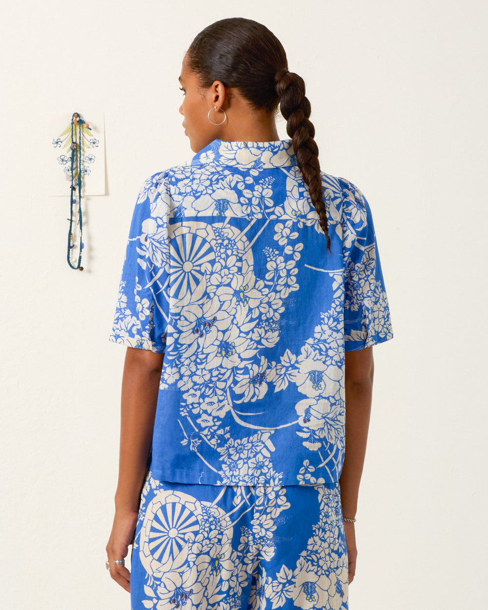 A woman with a braided hairstyle wears the Ophelia Royal Spoke Shirt and matching pants in blue and white, standing with her back to the camera.