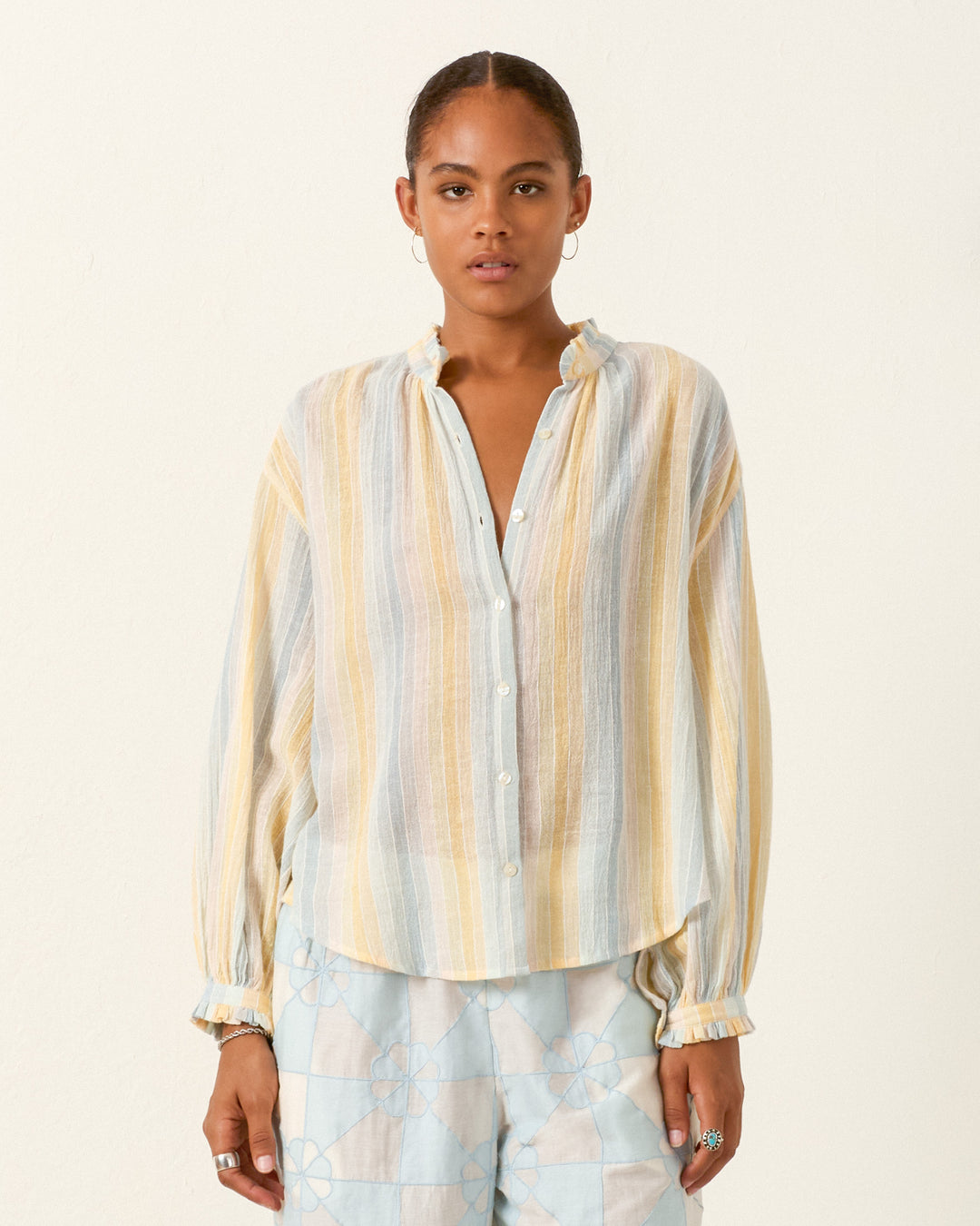 A person wearing the Poet Sunwash Stripe Blouse with long sleeves and pastel stripes stands against a plain light background.