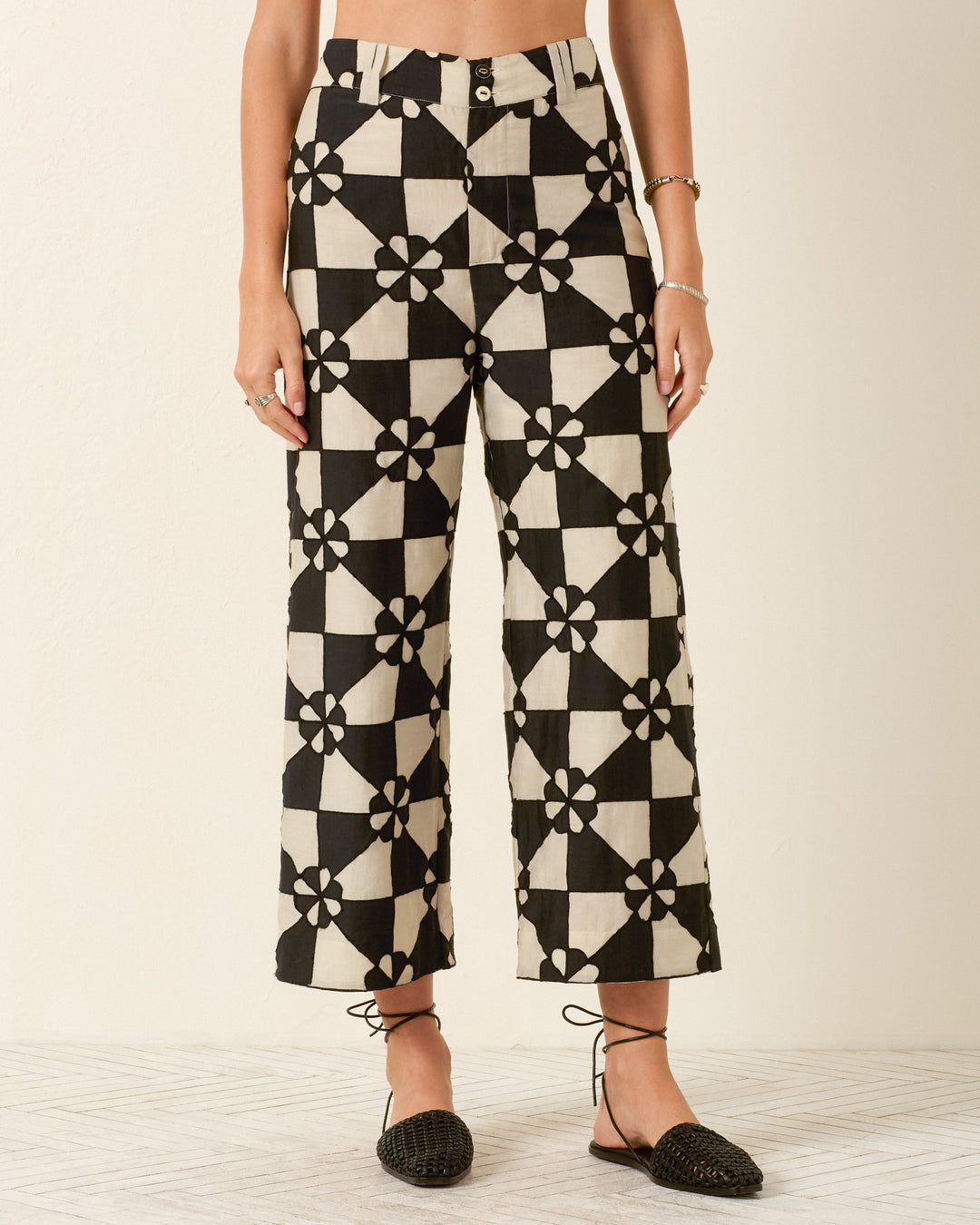A person wears the Scout Onyx Jubilee Pant—high-waisted, wide-leg pants featuring a black and white mosaic-inspired patchwork motif—paired with black woven sandals.