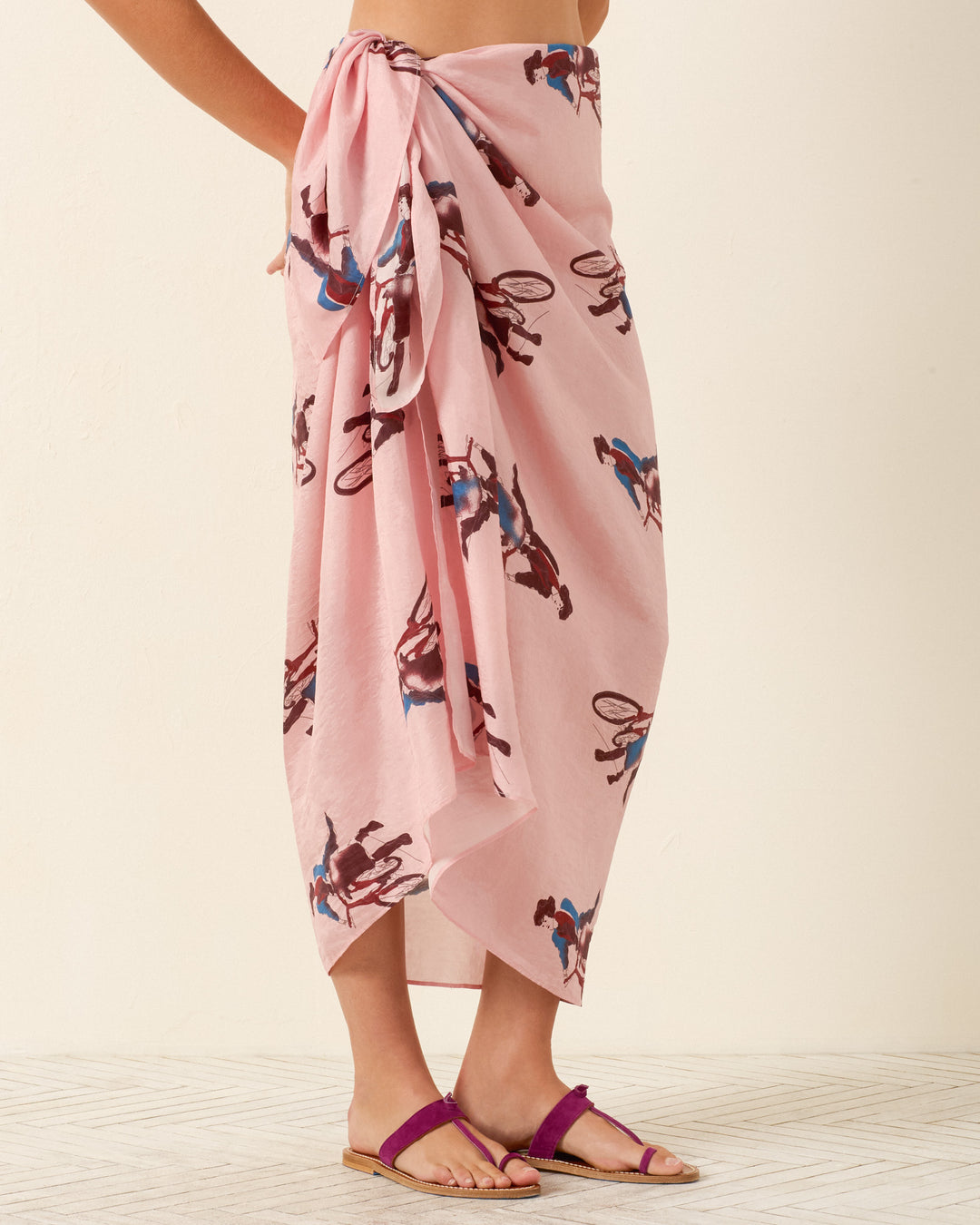 A person wearing the Soraya Parisian Pedal Sarong, featuring a hand-loomed silk horse and rider print, tied at the waist and paired with flat sandals.