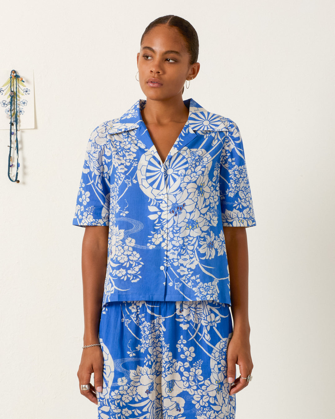 A person wearing the Ophelia Royal Spoke Shirt in blue and white stands against a plain white wall, paired with matching cotton voile pants.