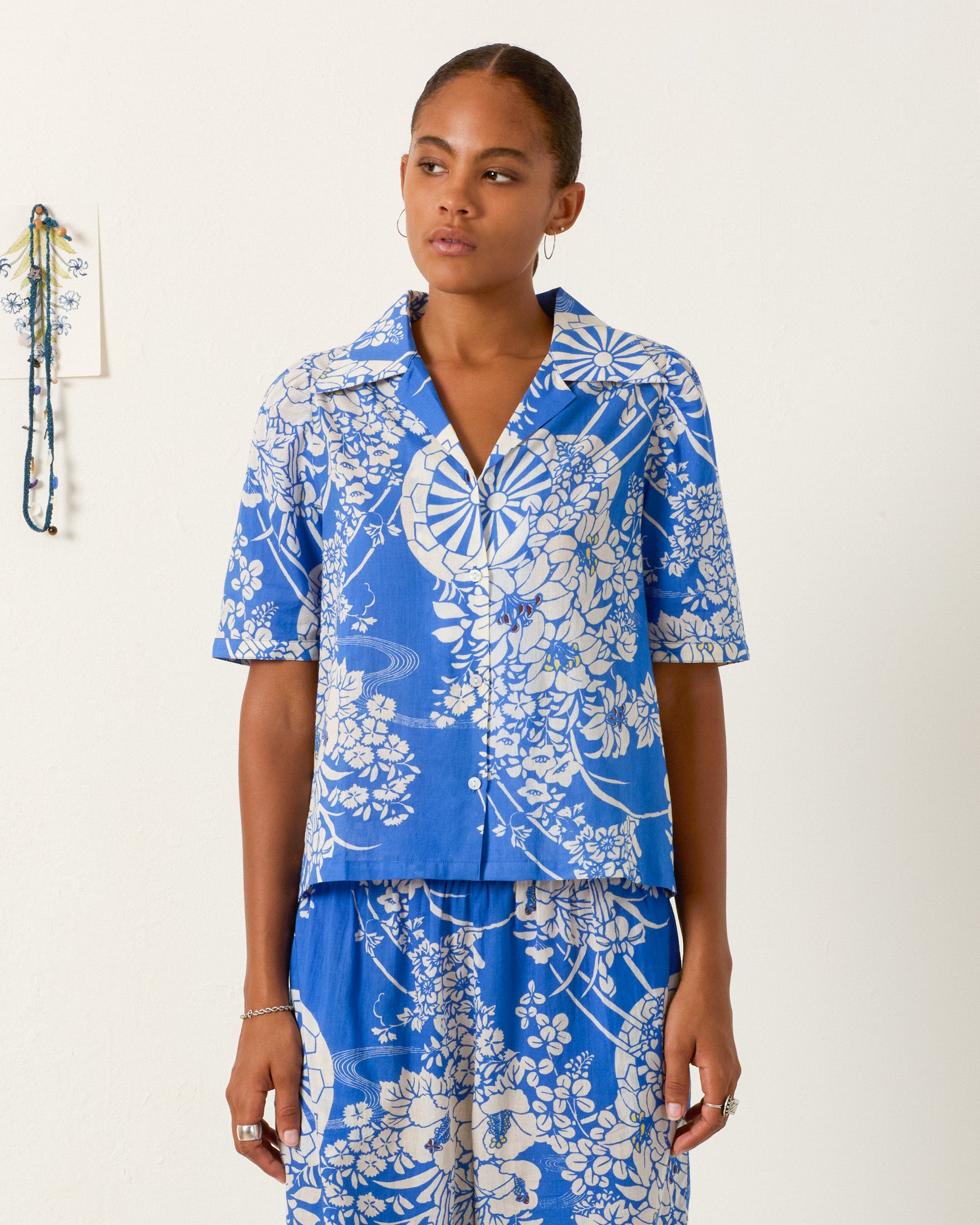 A person wearing the Ophelia Royal Spoke Shirt in blue and white stands against a plain white wall, paired with matching cotton voile pants.