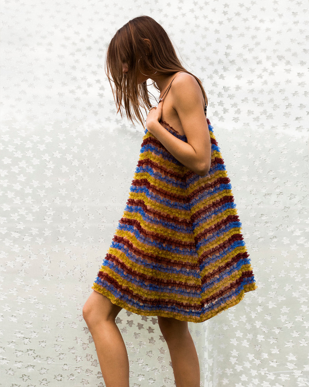 A woman wears the Soleil Jester Vale Dress, a sleeveless mini dress with multicolored stripes and textured fabric, standing against a white background featuring a subtle leaf pattern.